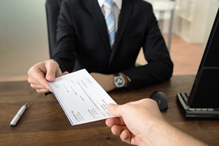 Close-up Of Businessman Hands Giving Cheque To Other Person In Office