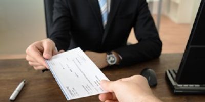 Close-up Of Businessman Hands Giving Cheque To Other Person In Office